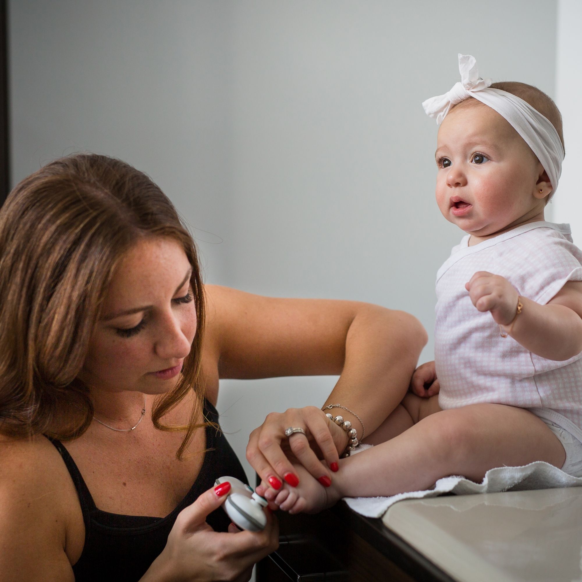 La Mère Utilise Un Coupe-ongles électrique Avec La Main De Bébé Sur Le Lit